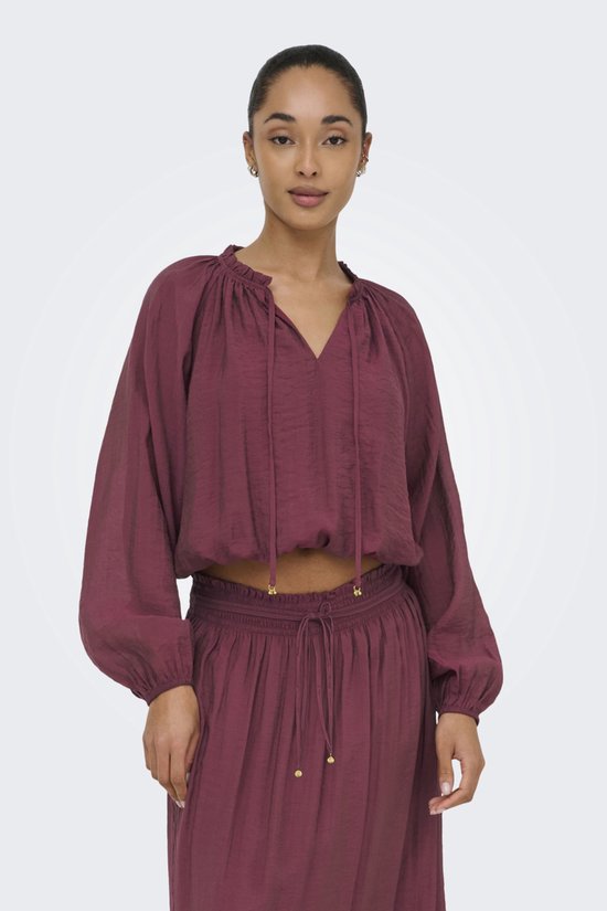 Model draagt een bordeauxrode crop top met pofmouwen en een v-hals met strikdetail. De top is gecombineerd met een bijpassende rok.