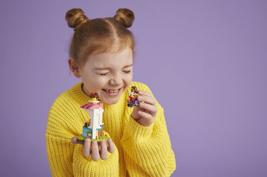 Fille aux couettes rousses et pull jaune rit en tenant des éléments de la Crêperie LEGO Friends.