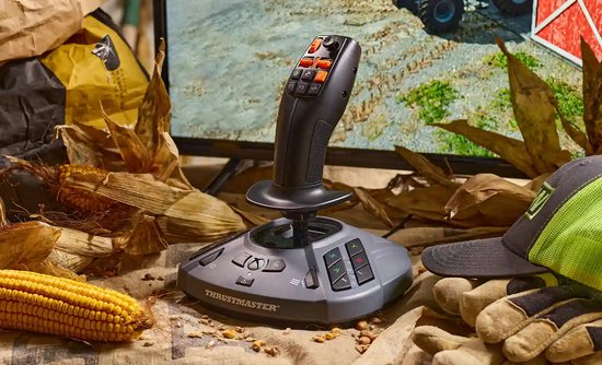 Zwarte joystick met oranje knoppen, deels op een console en deels in de lucht, omgeven door maïsplanten.