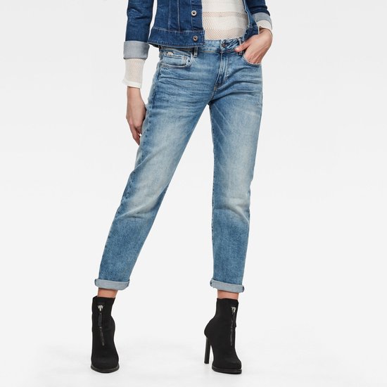Gedragen voorkant van een vrouw in een lichte, gescheurde jeans met opgerolde broekspijpen en zwarte laarzen.