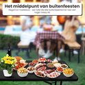 Een zwart tafelblad met rotan-look, vol met eten, op een buitenfeest.