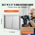 Een man met een boormachine monteert een 774x449 mm RVS BBQ keuken deur. De afmeting 27"/689 mm breed en 18"/449 mm hoog is aangegeven.