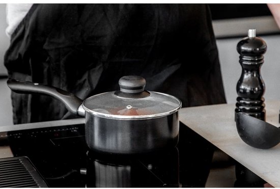Casserole noire Masterclass avec couvercle en verre sur une plaque de cuisson, à côté d'un moulin à poivre.
