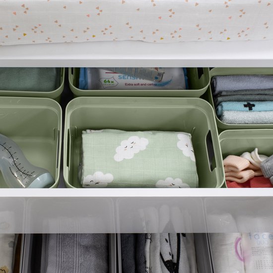 Groene opbergboxen met daarin babykleding, luiers en een fles, netjes in een lade gerangschikt.