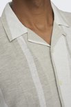 Close-up van een beige kortarmig overhemd met verticale beige en witte strepen.