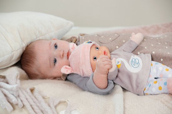 Baby ligt op haar rug, met een popje naast haar. Het popje draagt een roze muts met oortjes en een grijs shirt met zwaan.