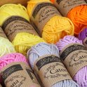 Close-up van diverse kleuren Scheepjes Catona garen, waaronder geel, roze, paars en grijs.