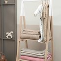 Babykleertjes hangen aan een rek met daaronder op de planken geweven dekens in beige en roze.