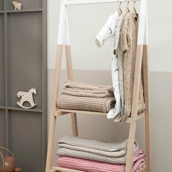 Babykleertjes hangen aan een rek met daaronder op de planken geweven dekens in beige en roze.