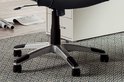 Base d'un fauteuil de direction noir avec cinq pieds argentés et roulettes noires sur un tapis gris.