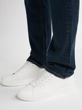 Onderlichaam van man in donkerblauwe jeans en witte sneakers.