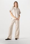 Model draagt een beige linnen blouse met korte mouwen en wijde broek.