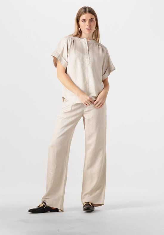 Model draagt een beige linnen blouse met korte mouwen en wijde broek.