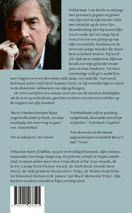 Man met grijze haren en baard, gekleed in een grijs pak. Ligt op een sofa met een boek in zijn handen.