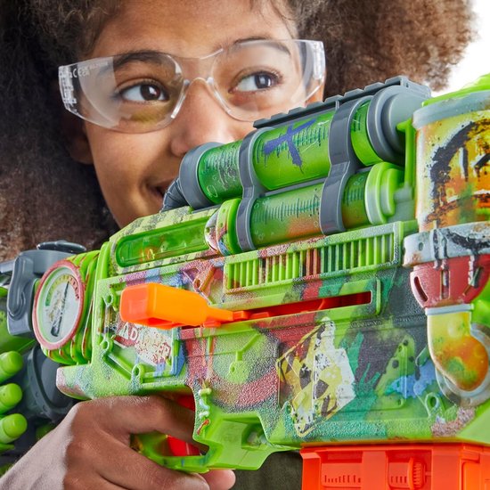 Meisje met beschermende bril houdt een felgroene Nerf Zombie Corrupter blaster vast, versierd met zombie-thema afbeeldingen.