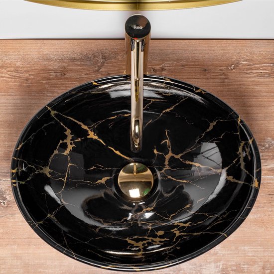 Vue de dessus d'un lavabo ovale noir avec imprimé marbre et veines dorées, robinetterie dorée.