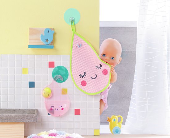 Baby pop achter roze druppelvormige badmat. Gele badeend op de voorgrond. Roze beker met speelgoed aan muur.