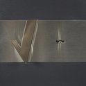 Close-up van een metalen plaat met zilverkleurig 'V'-logo en sleutelgat op een grijze kluis.