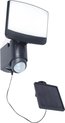 Donkergrijze wandlamp met sensor en apart zonnepaneel op wit voorgesteld.