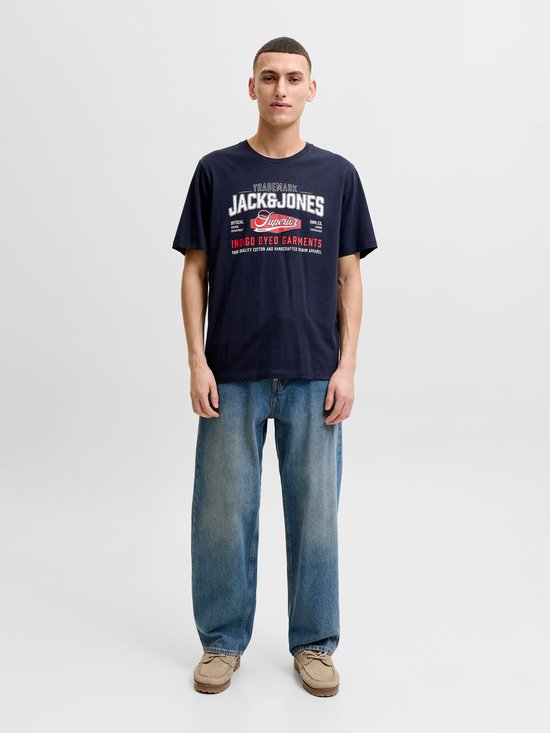 Man in marineblauw T-shirt met wit-rode 'JACK & JONES' print en wijde spijkerbroek.