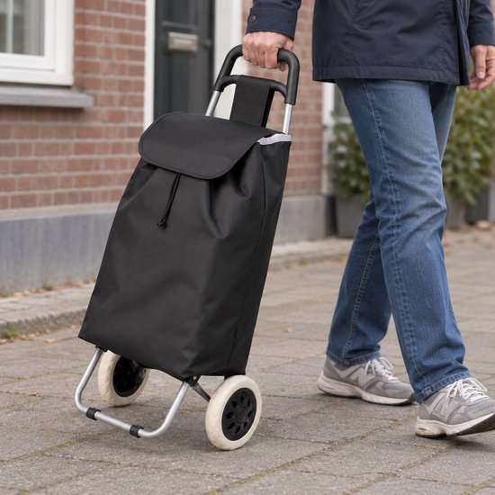 Persoon die de zwarte boodschappentrolley voorttrekt op een straat.