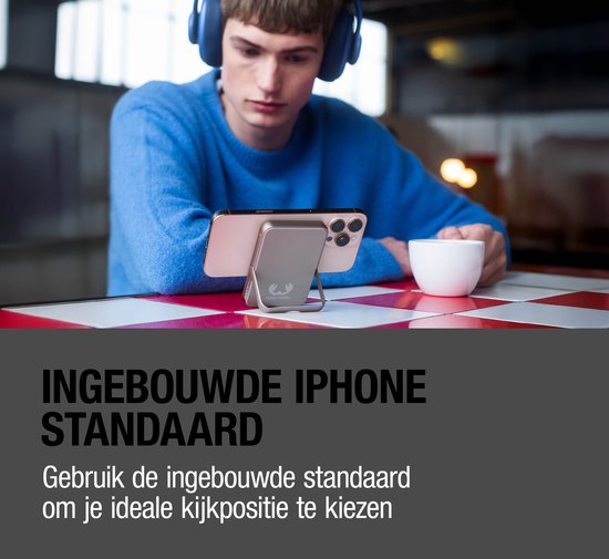 Een jonge man met koptelefoon gebruikt een telefoon met ingebouwde standaard, die opgeladen wordt door een magnetische powerbank.