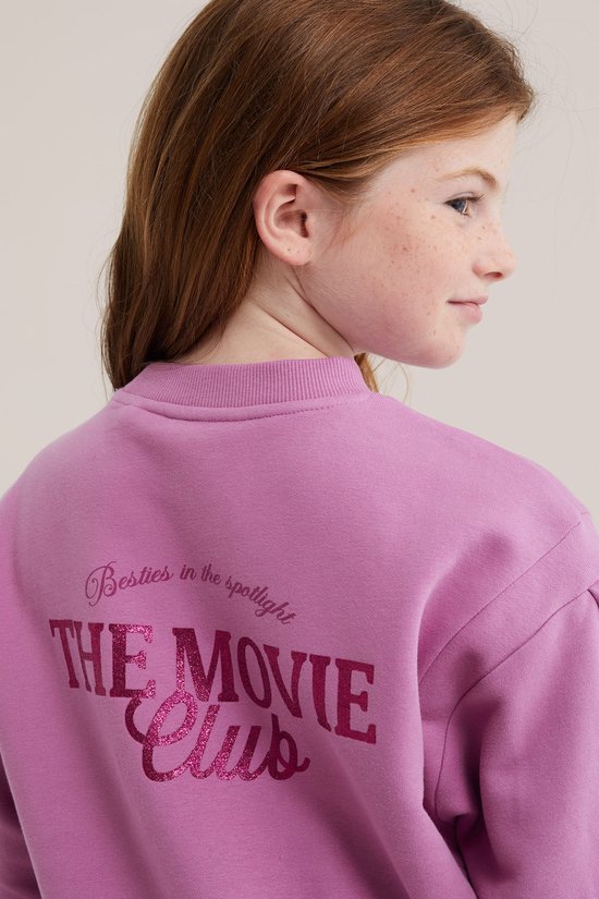 Achterkant van een roze sweaterjurk met de tekst "Besties in the spotlight THE MOVIE Club" in glinsterende letters.