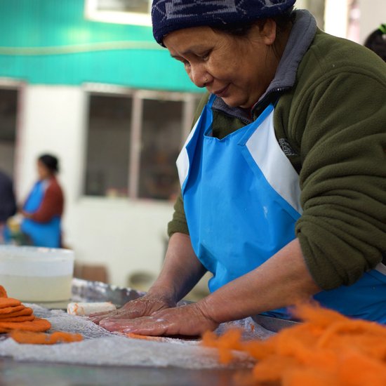 Vrouw met blauw schort werkt met oranje vilt.
