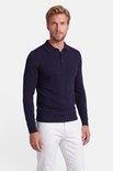 Model in een marineblauwe polo met lange mouwen en een witte broek.