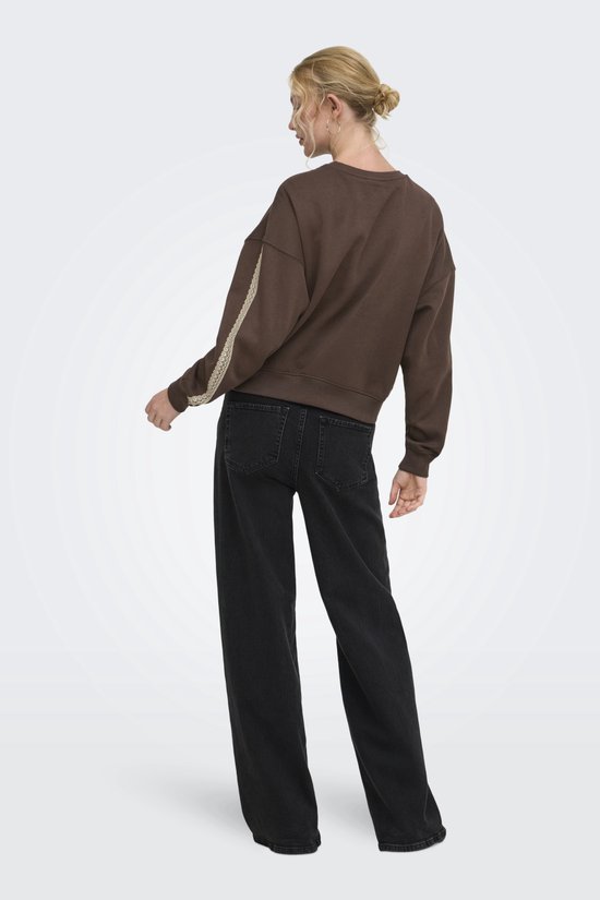 Aanzicht op de rug van een model in een bruine trui met kanten details op de mouwen en een zwarte broek.