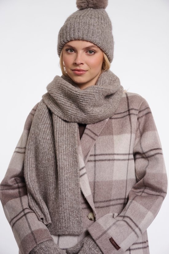 Portret van model met beige geruite jas, grijze muts en sjaal met label 'HANDMADE'.