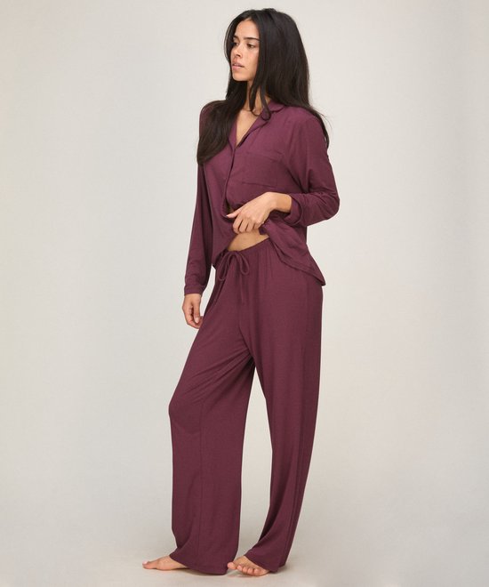 Model draagt een bordeauxrode pyjamaset met een pyjamabroek met trekkoord en een bijpassend shirt met knopen.