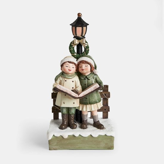Deux figurines de Noël d'enfants en tenue d'hiver lisant ensemble sous un lampadaire orné d'une couronne.