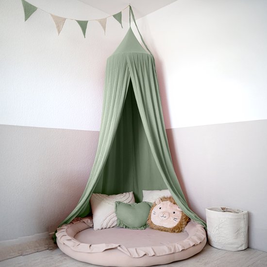 Groene mousseline klamboe met gouden accenten en bijpassend rond speelkleed met leeuwenkussen in kinderkamerhoek.