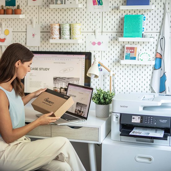 Vrouw in lichte kleding houdt een bruine kartonnen doos met 'EcoPro' logo vast, zittend aan een bureau met een printer en laptop.