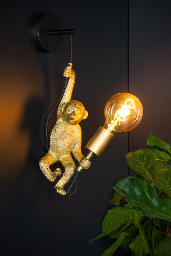 Gouden wandlamp in de vorm van een aap die aan een touw hangt en een lichtgevende gloeilamp vasthoudt.