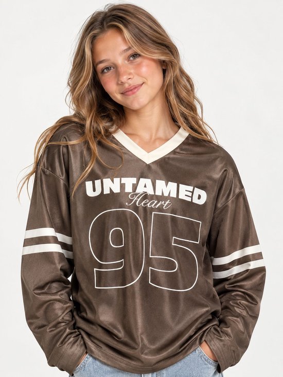 Bruin sportief V-hals shirt met lange mouwen, met 'UNTAMED Heart 95' op de voorkant en witte strepen op de mouwen.
