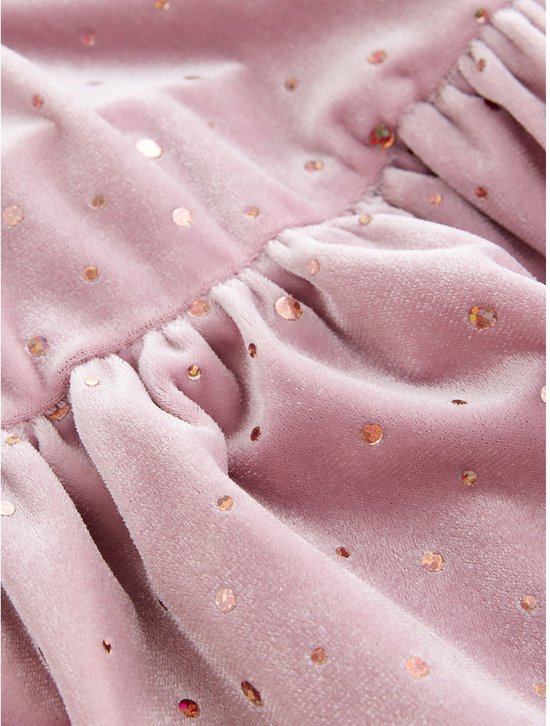 Close-up van een roze fluwelen jurk met rimpeldetails bij de naden en versierd met glinsterende pailletten.