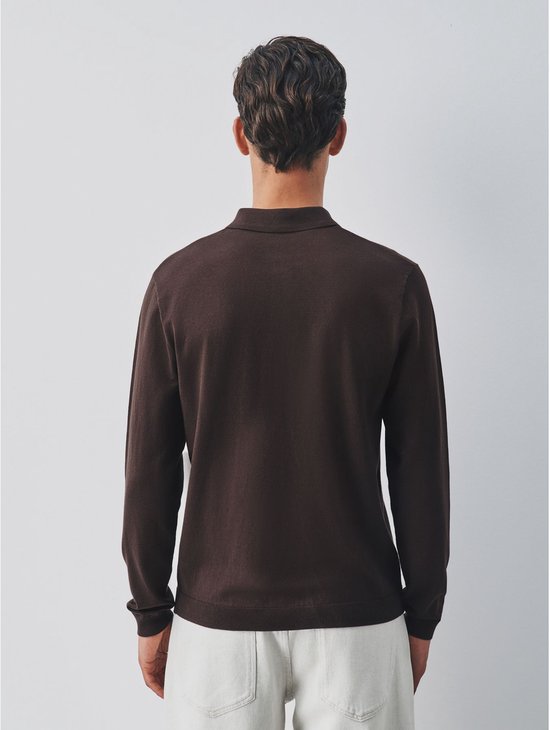 Achterkant van een bruin gebreid poloshirt met lange mouwen, gedragen door een man met lichtgekleurde broek.