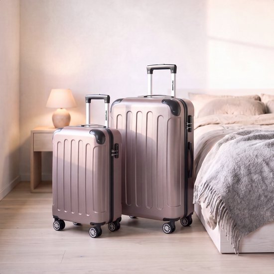 Twee roze koffers, een handbagage en een grote ruimbagage, in een slaapkamer naast een bed.