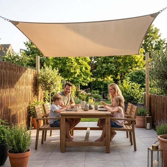 Een gezin eet aan een tafel onder een beige vierkant schaduwdoek op een betegeld terras.
