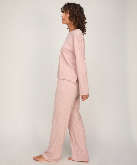 Model in profiel, draagt een zachtroze pyjamaset met longsleeve top en een broek met een print van witte hartjes.