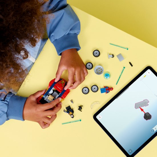 Kind bouwt rode raceauto met blauwe en gouden accenten, naast een tablet met instructies.