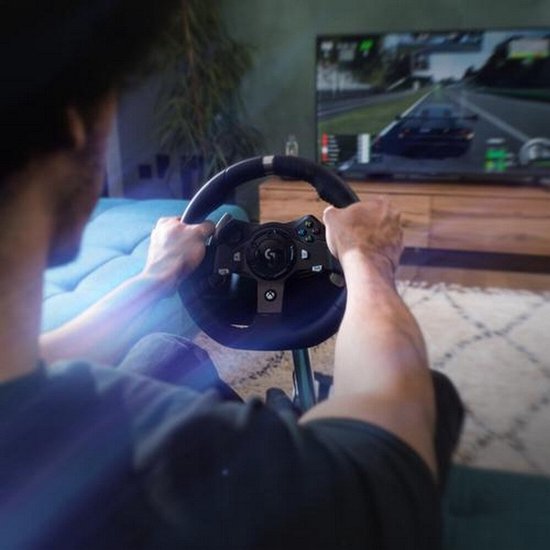 Persoon gebruikt een Logitech G-stuur in een woonkamer met racespel op de achtergrond.