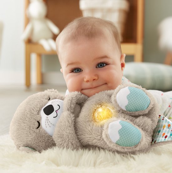 Een lachende baby ligt op een witte vacht met een bruine otter knuffel.