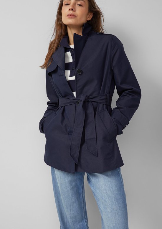 Model draagt donkerblauwe s.Oliver outdoor jas met ceintuur, gestreepte top en spijkerbroek.