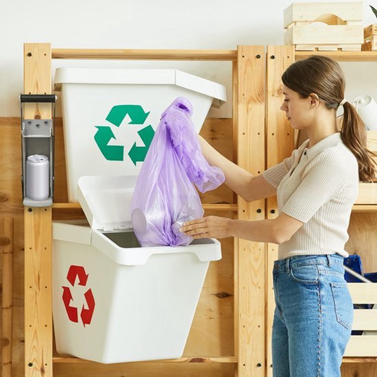 Vrouw plaatst een paarse vuilniszak in een witte prullenbak naast een aan de muur gemonteerde blikbreker met blikje.