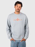 Model in een lichtblauwe Brunotti sweater met een oranje grafisch logo, gecombineerd met een jeans.