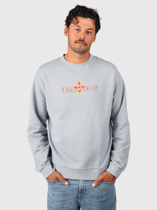 Model in een lichtblauwe Brunotti sweater met een oranje grafisch logo, gecombineerd met een jeans.
