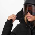 Vrouw sluit de capuchon van haar zwarte ski-jas, met paarse skibril en helm.